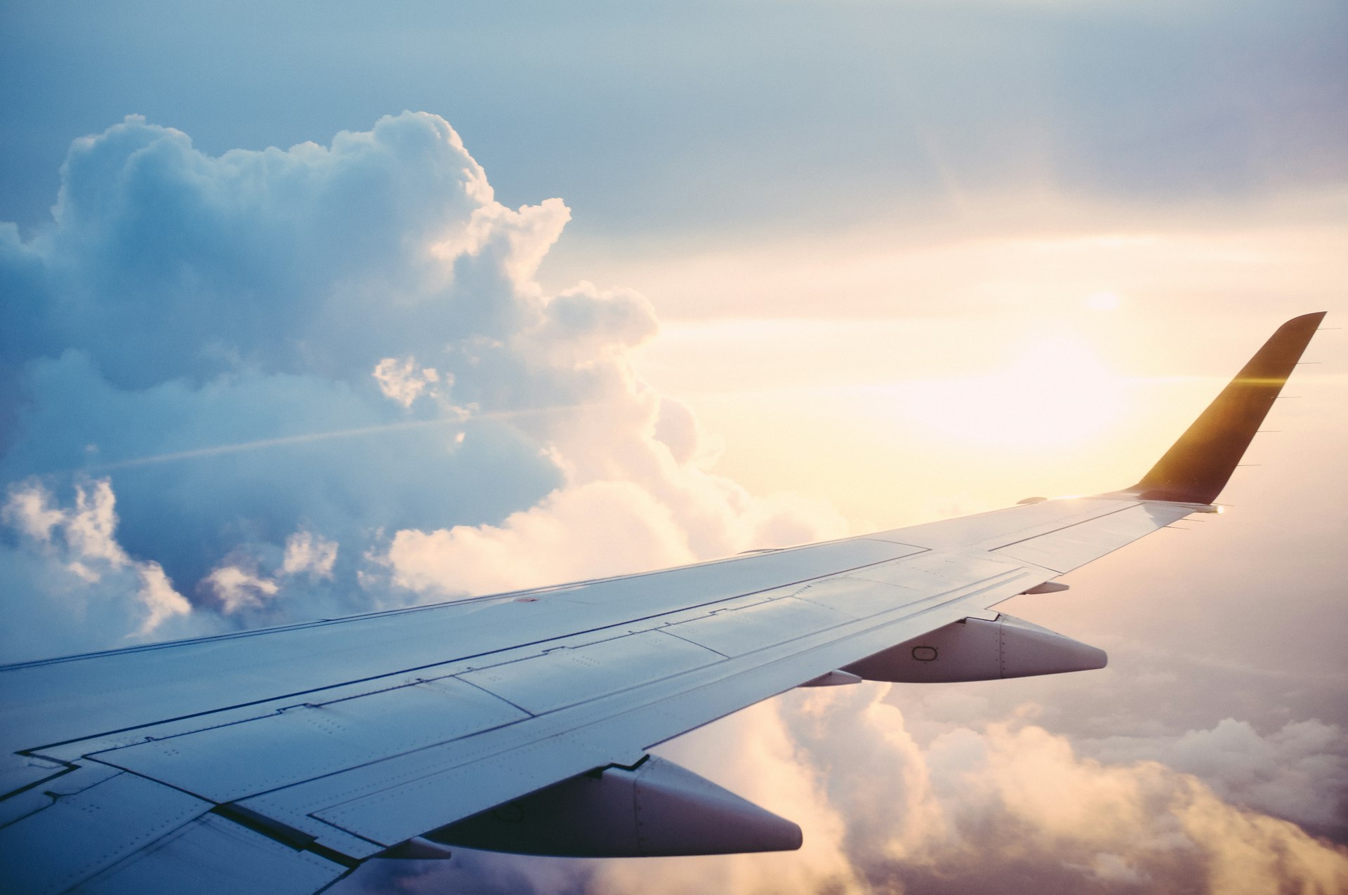 View of airplane wing flying above clouds during sunset