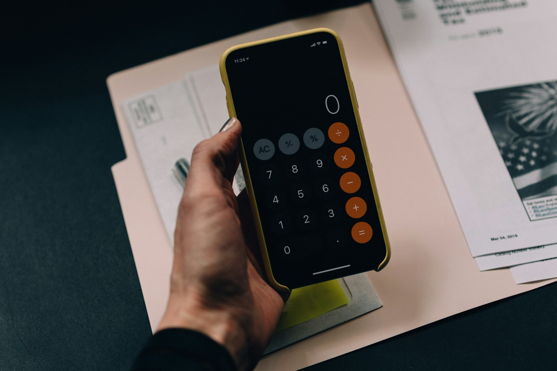 Calculator app on smartphone with financial documents in background