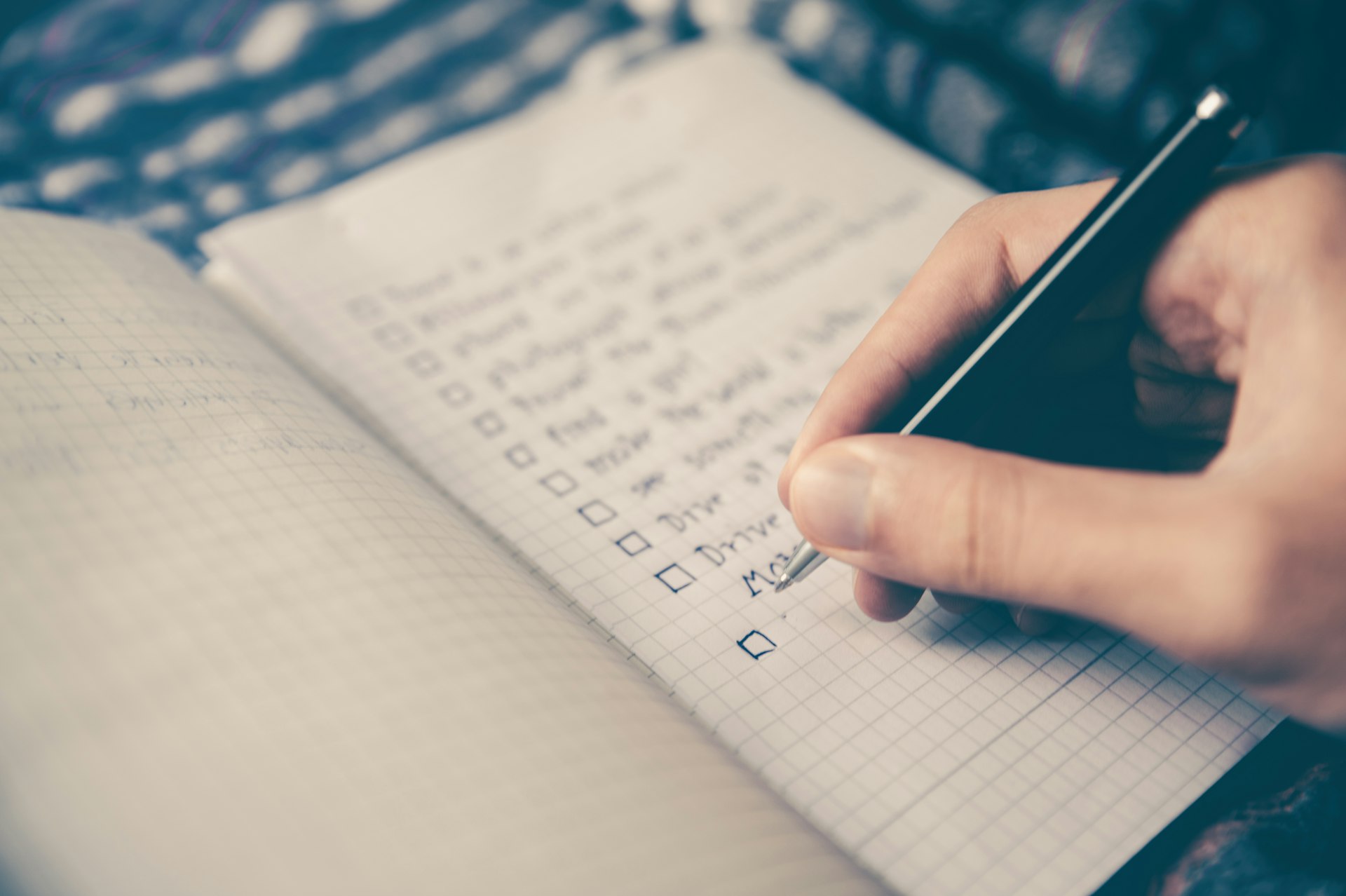 Hand holding smartphone while checking items off a checklist in a notebook