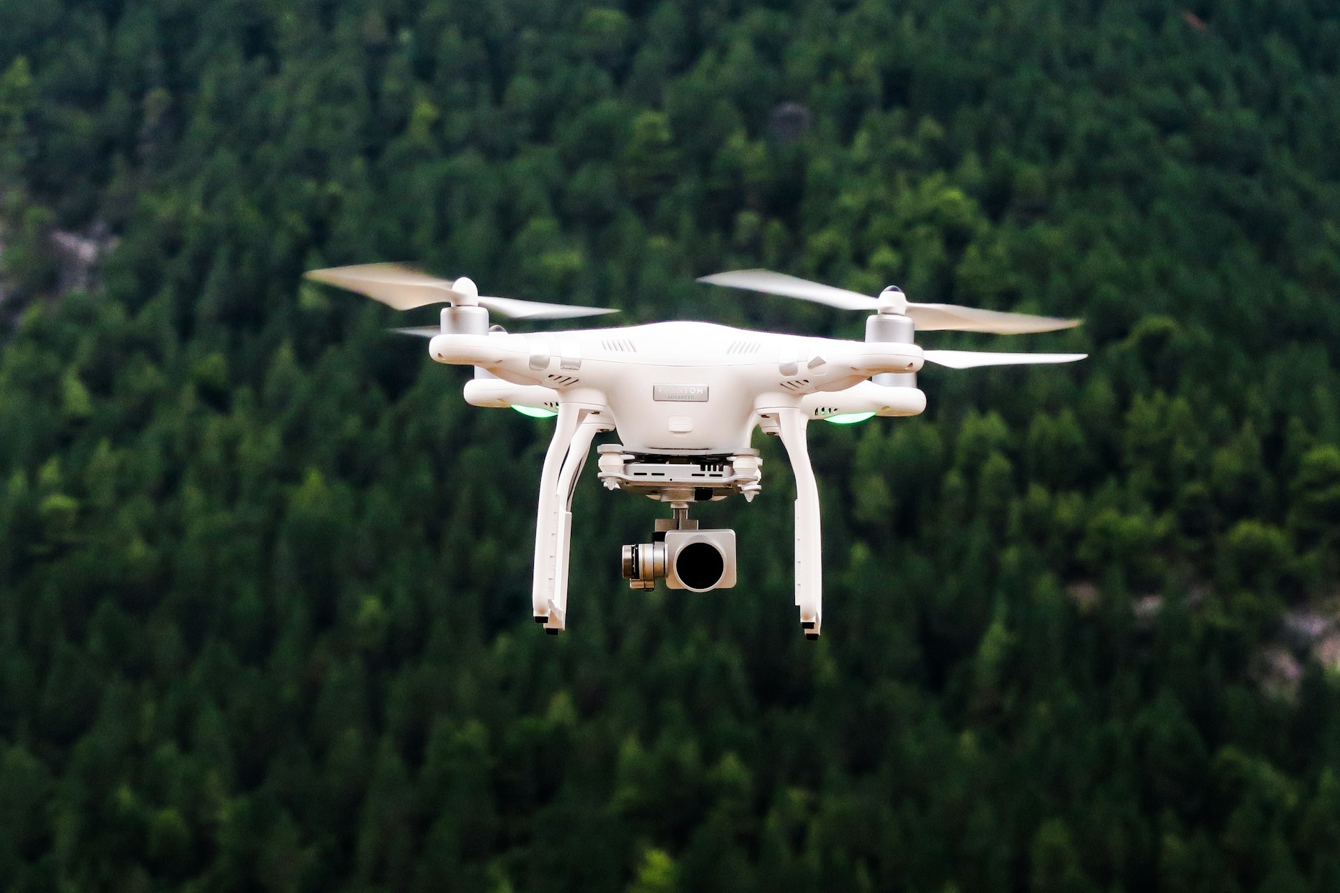 White quadcopter drone flying against green forest background